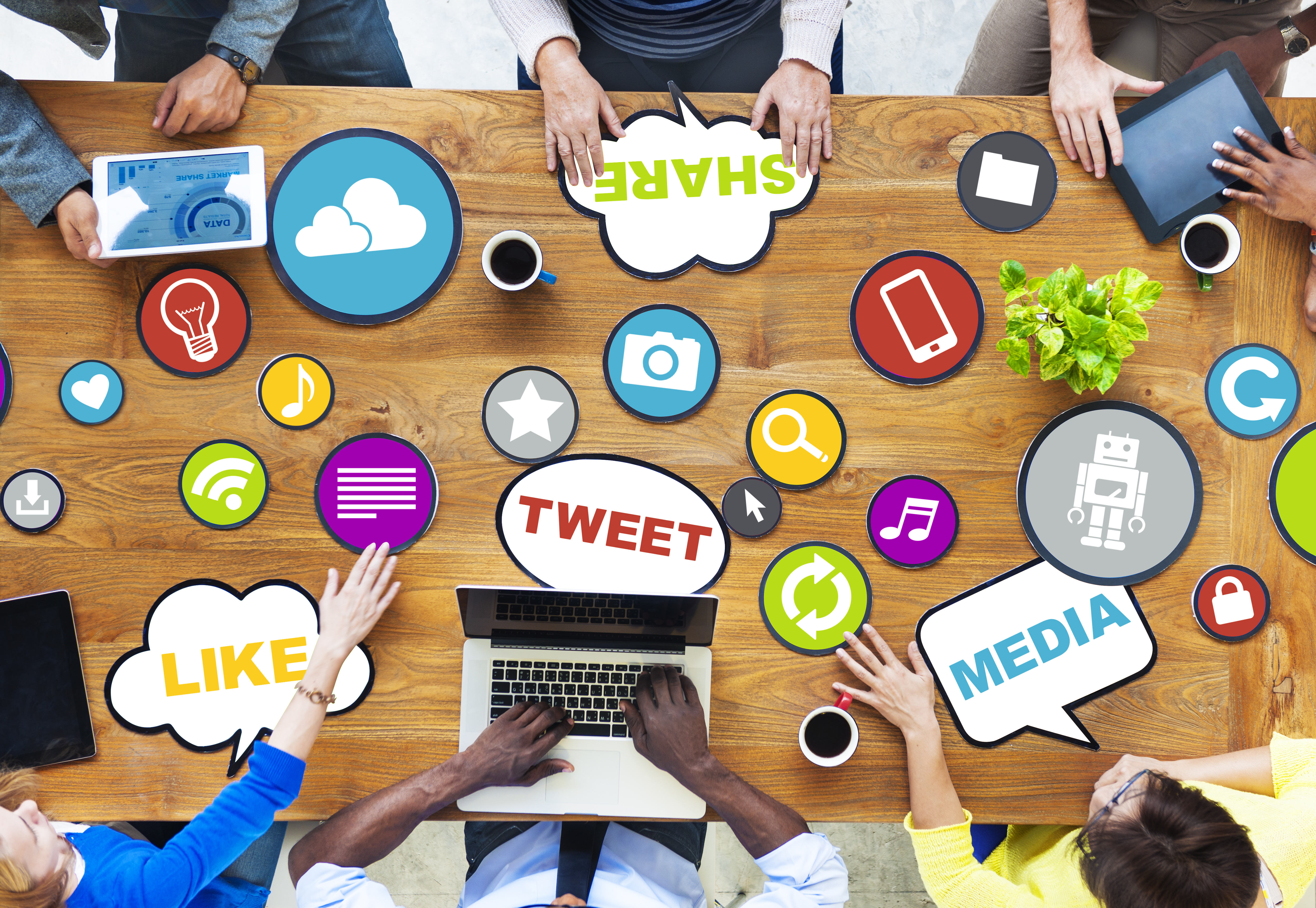 Various social media icon image (for example cameras or tweets) cut outs lying on a desk with people looking down on them